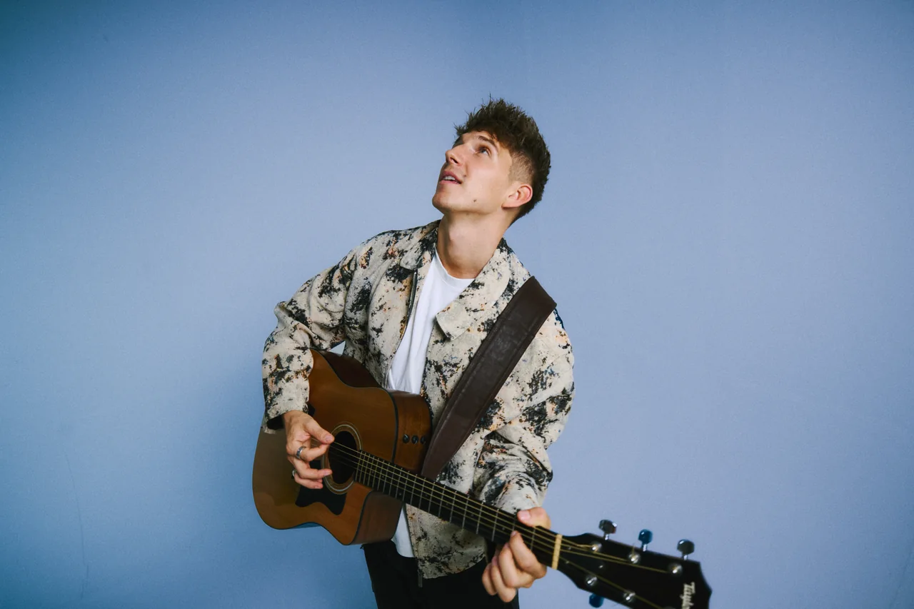 Toni Mogens mit Akustikgitarre vor blauem Hintergrund